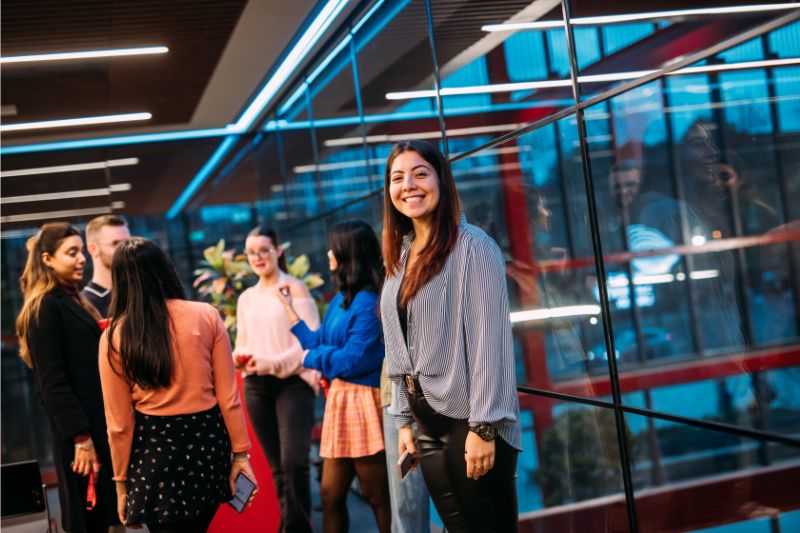 female student standing in a room next to a crowd of students